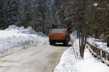 Orange-coloured Snowplough Operating on the Road with Snow on the Edges