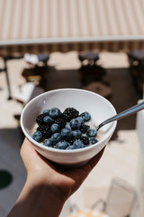 Female hand holding bowl with oatmeal and blueberries. Tasty and helthy breakfast outdoor. 