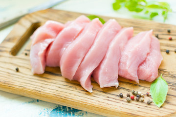 Raw meat fillet of turkey, chicken sliced on a wooden board.
