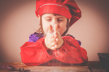 Concept of homemade cooking. Hands of little cute child girl chef clapping and sprinkling white...