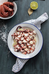 Overhead view of two dishes full of delicious octopus, one sliced and main focused, with olive oil on top and a potato bed, the other includes four arms on it and the scissors that cut it.