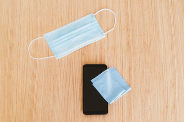 Top view of smartphone being sanitize with wipe cloth. Protective face mask to prevent contagious covid 19 coronavirus disease. Disinfect electronic devices and stay home. Hygienic recommendation.