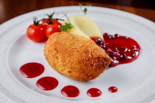 Kiev chicken cutlet with mashed potatoes and berry sauce on a white plate.