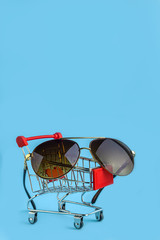 Travel concept shopping cart with sunglasses on blue background.