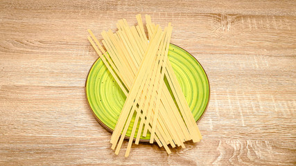Uncooked raw linguine pasta on a green plate on wood background. Top view, vertical photo, selectiv focus, with copy space, space for text.
