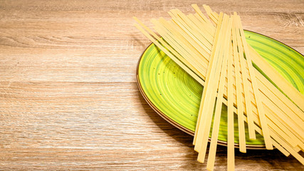 Uncooked raw linguine pasta on a green plate on wood background. Closeup, Top view, vertical photo, selectiv focus, with copy space, space for text.