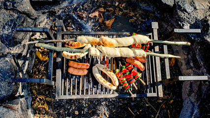 Assorted grilled vegetables, sausages and bread over a barbecue grid fire place, shot from top