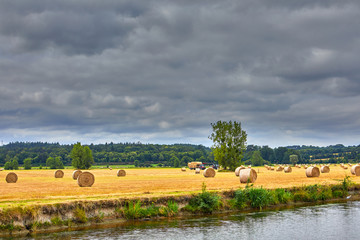 Image of an a field with straw rolls with tractors and the vilaine river in the foreground.