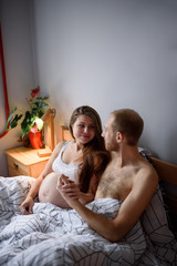 Obraz na płótnie Canvas Pregnant couple during quarantine have fun in their bed.