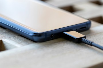 A close up portrait of a smartphone with a USB cable in its port. It is either charging or connected to something like a computer to transfer data.