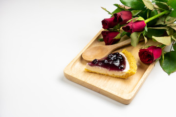 Blueberry Cheesecake with blueberry jam on wooden plate and red rose flowers on white background.