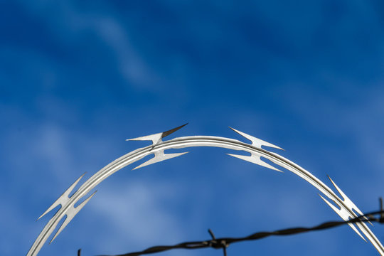 Close up of coils of razor wire on a security fence against a deep blue sky