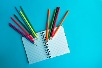 Colored pencils with a Notepad on a blue background