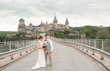 Obraz premium Stylish bride and groom. Just merried. wedding couple.Close up. Happy bride and groom on their wedding day. Groom and Bride walking near old castle. wedding dress. Bridal wedding bouquet of flower