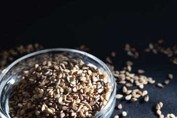 Close-up of Organic whole sesame seeds, in a small glass bowl on a black background