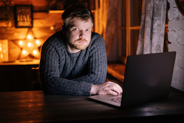 Portrait of caucasian young man sitting at the table with laptop and looking at the camera. Concept of remote working from home.