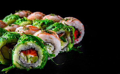 set of Sushi rolls with seafood, srimp, cream cheese,caviar and Chuka salad on black wooden table background