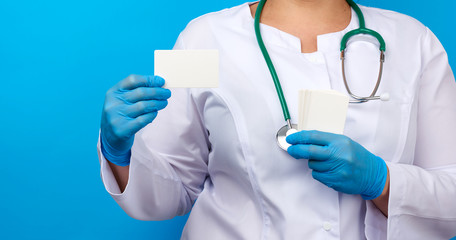 female doctor hand in blue medical latex gloves holds an empty paper business card on a blue background