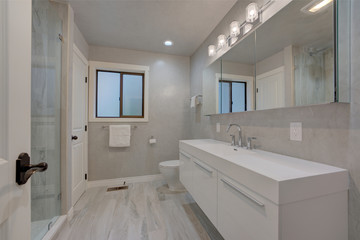 New modern bathroom interior grey venetian plaster, grey tiles, shower with glass walls, slick white shiny venity.