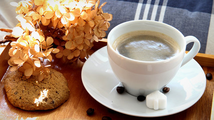 Homeoffice during the coronavirus outbreak concept - a closeup of wooden tray with cup of coffee, cookies and hydrangea flower on bed selective focus