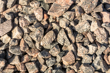 Wallpaper with gravel. Stone background. Texture of stones on a road lit by bright sunlight. Gravel texture. Building material for the road.