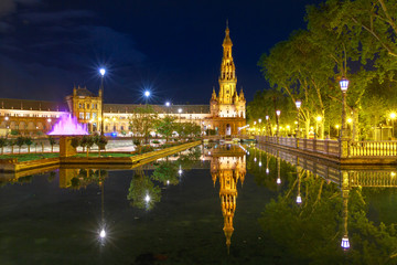 Obraz premium Scenic panorama of Spain Square in Andalusia, Spain, illuminated at night. Renaissance building and one of two towers in Plaza de Espana reflects on canal of Guadalquivir river in Seville.