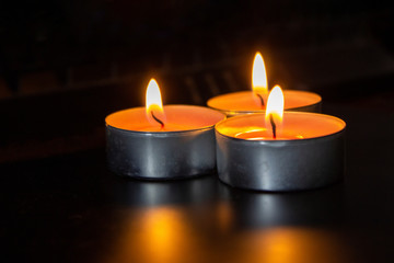 Obraz na płótnie Canvas Composition of three candles on dark luxury night background. Black table, side view. Candles Burning at Night. Orange taper burning in focus, foreground. illustration design.