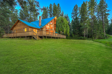 Luxury summer mountain cabin home with large green lawn and pine trees.