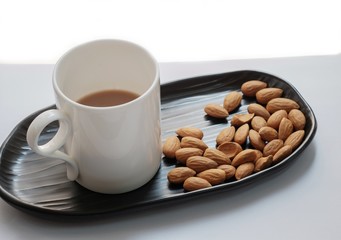 The coffee in a white cup and almond on a black tray.