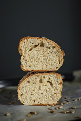 A homemade bread cut in half, one half on top of another, covered in sunflower seeds, on baking paper, vertical photo