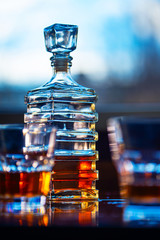 Glass of whiskey with old square carafe on a wooden table