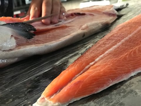Peixe salm&atilde;o cru, sendo limpado e cortado com fundo desfocado