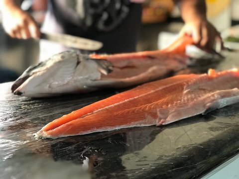 Peixe salm&atilde;o cru, sendo limpado e cortado com fundo desfocado