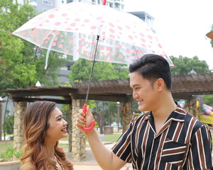 Young Asian Malay man woman couple outdoor green park walk talk discuss mingle under umbrella