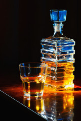 Fototapeta na wymiar Glass of whiskey with old square carafe on a varnished wooden table