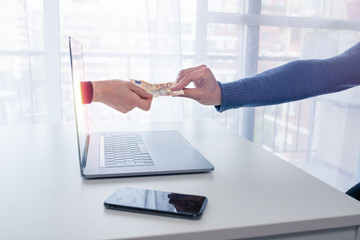 Online transaction. An arm comes out of a laptop to collect money from a customer or taxpayer. It...