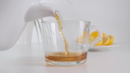 Pour hot tea on glass cup. White teapot. Slow motion.