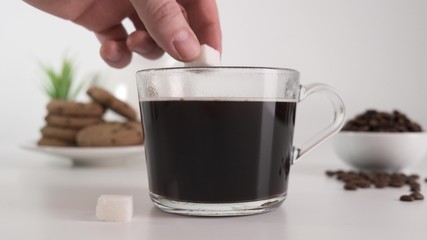 Female hand dropping a sugar cube into the glass cup coffee. Slow motion.