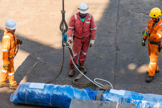 Stevedore Crews Preparing To Lift Pipe Spool From Wharf To A Construction Work Barge