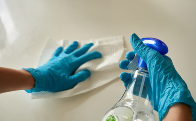 Human hands wearing blue disposable latex glove cleaning the white surface with a white paper towel...