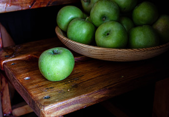 
green apple on a brown wooden chair on a dark background, a wooden plate with green apples