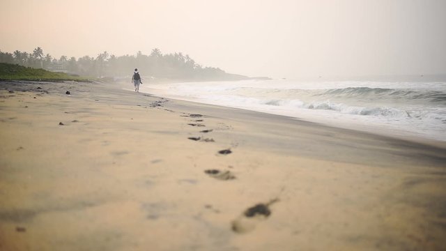 Footprints Of A Man With A Backpack Walking In The Seashore Of Varkala Beach In India. -wide shot