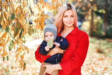 A stylish young mother with a small son in her arms walks in the autumn.