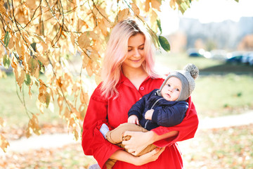A stylish young mother with a small son in her arms walks in the autumn.