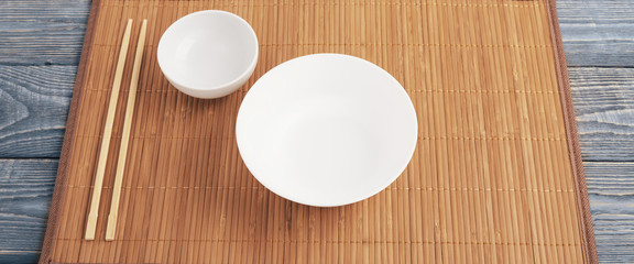 Two wooden chopsticks and two white cup bowl on a bamboo mat