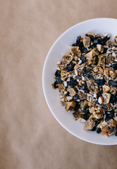 Half of white bowl with homemade granola on parchment paper background. 