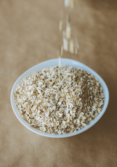 Pouring oatmeal into white plate. Ingredients for cooking breakfast or granola. Parchment background.