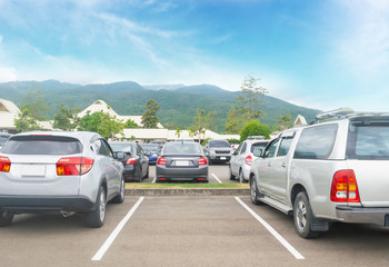 Fototapeta na wymiar Car parked in asphalt parking lot and one empty space parking in nature with trees, beautiful cloudy sky and mountain background .