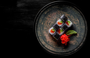 sushi roll with salmon, avocado, rice in plate on black wooden table background