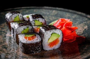 sushi roll with salmon, avocado, rice in plate on black wooden table background